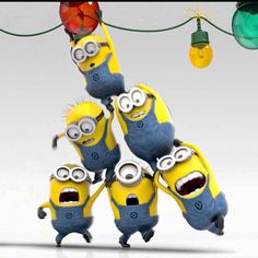 three minion characters hanging from a string with christmas lights in the background and decorations