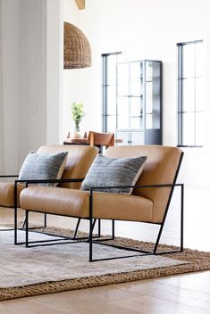 two brown leather couches sitting on top of a rug in front of a window