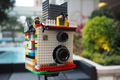 a toy camera is made out of legos and sits on a tripod in front of a pool