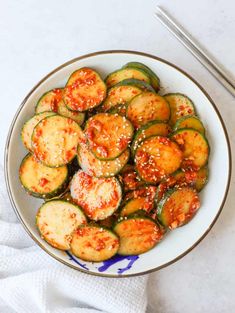 a bowl filled with zucchini and sauce next to two chopsticks on the side