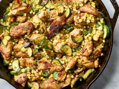 a skillet filled with chicken, corn and zucchini on top of a table