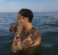 a man with tattoos on his body sitting in the water and covering his face with his hands