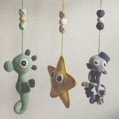 three crocheted toys hanging from strings in the shape of animals and stars on a white wall