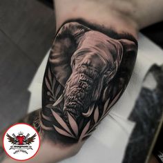 an elephant tattoo on the left arm and leg, with leaves around its head in black and grey ink