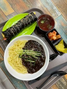 a tray with noodles, sauces and other foods on it next to chopsticks