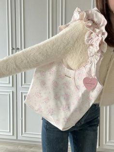 a woman holding a white purse with pink flowers on it and a heart shaped tag