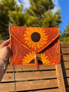 a woman's hand holding an orange leather purse with sunflowers on it