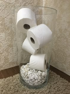 three rolls of toilet paper are stacked in a glass vase filled with rocks and pebbles