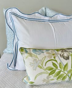 two pillows on top of a bed with blue trimmings and green flowers in the middle