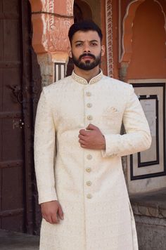 This off white / cream Sherwani has a distinctive mandarin collar and a row of buttons down the front. It features long sleeves and has a golden woven pattern on it. The matching churidar pants are also made with the same golden woven design.  The Sherwani is made of imported fabric and is available in off white / cream colour. The package includes the Sherwani, Churidar pants (which are styled without any specific design)  This elegant Sherwani suit is ideal for formal events, parties and evening dinners. Customization options are available for size, design and colour to suit your personal style and taste. We can also give you a turban, jooti, mojari of your matching outfit (additional cost will be apply). For your comfort and best fit we keep 2 Inches Extra Margin in the dress, please pr Formal Sherwani For Men, Lakhnavi Sherwani For Men, Sharvani For Men Wedding White, Cream Colour Sherwani For Men, Cream Sherwani Grooms, Formal White Raw Silk Traditional Wear, Ceremonial Cream Bandhgala With Cutdana, White Raw Silk Long Sleeve Sherwani, Ceremonial Cream Bandhgala With Chikankari Embroidery