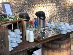 a table with cups and saucers on it next to a wooden barrel filled with flowers