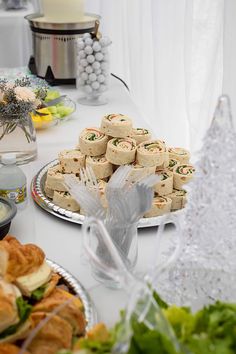 a table filled with sandwiches and pastries on silver platters next to other food items