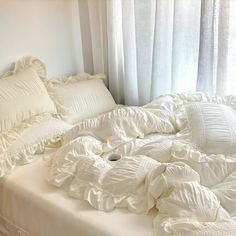 an unmade bed with white ruffled sheets and pillows on the bottom, in front of a window