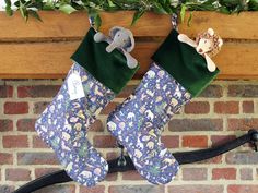 two christmas stockings hanging from a fireplace with stuffed animals on them and greenery in the background