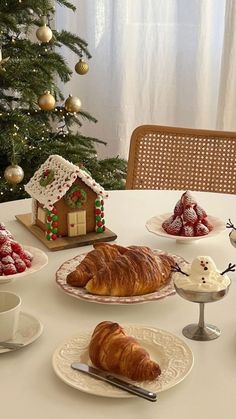 a table topped with croissants and pastries next to a christmas tree