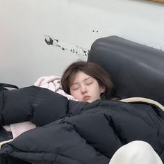 a woman sleeping in a black jacket on top of a bed next to a white wall