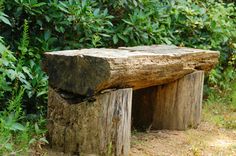 a wooden bench made out of logs sitting in the middle of some grass and bushes