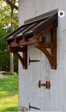 an old white shed with a metal roof and wooden brackets on the front door frame