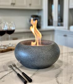 a bowl with flames in it sitting on top of a counter next to wine glasses