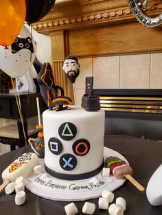 a birthday cake decorated with video game controllers and marshmallows on a table