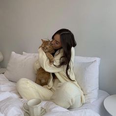 a woman sitting on a bed with a cat in her lap and she is holding the cat up to her chest