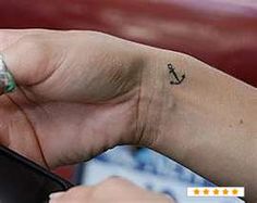 a person with a small anchor tattoo on their left wrist and right hand holding a cell phone