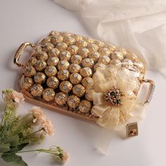 a gold tray filled with lots of chocolates on top of a white table next to flowers