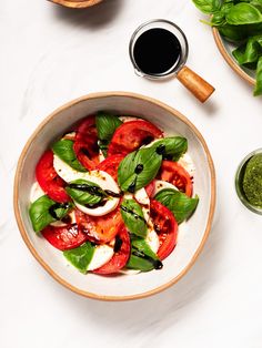 a white bowl filled with tomatoes and basil next to some pesto on the side