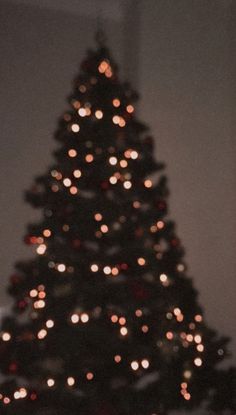 a lit up christmas tree in front of a white wall with red and gold lights