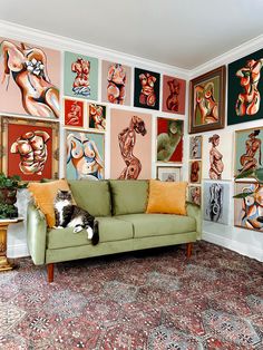 a living room filled with lots of paintings on the wall and a cat laying on top of a couch