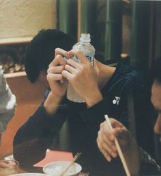 a person sitting at a table with chopsticks and a bottle