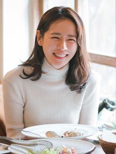 a woman sitting at a table with plates of food in front of her and smiling