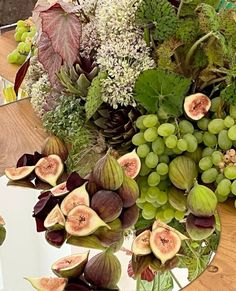 an arrangement of fruits and flowers on a table with mirrors in the background, including figurines