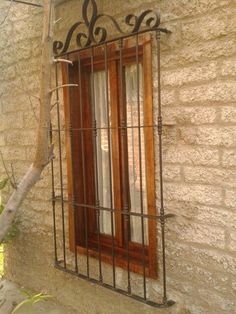 a window with iron bars on the side of a stone building next to a tree