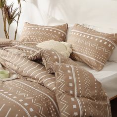 a bed with brown and white comforter next to a potted plant on top of it