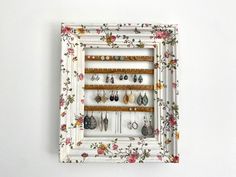 a white frame holds several pairs of earrings and earring hooks, with flowers on it