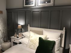 a white bed topped with lots of pillows next to a night stand and two pictures on the wall