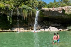 two people standing in the water near a waterfall