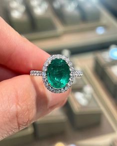 a close up of a person's hand holding an emerald and diamond ring