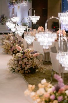 the tables are lined up with flowers and chandeliers