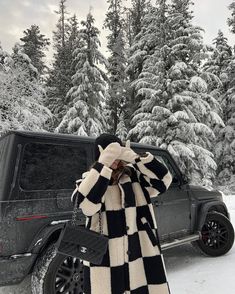 a woman standing in front of a black and white checkered coat on top of snow covered ground