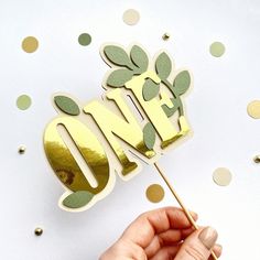 a hand holding a cake topper with the word love spelled out in gold foil