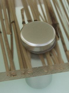 a metal object sitting on top of a glass table with wooden sticks in the background