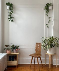 two wooden chairs sitting next to each other in front of a wall with plants on it