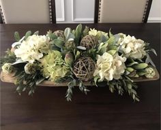 a wooden tray with white flowers and greenery on top of a dining room table