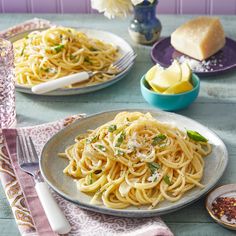 two plates of pasta with parmesan cheese and herbs on the table next to some flowers