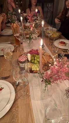 people sitting at a dinner table with plates and glasses on it, candles in the middle