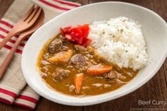 a white bowl filled with meat and rice next to a fork on top of a wooden table