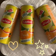 three cans of lipton peach tea on a bed with hearts drawn in the background