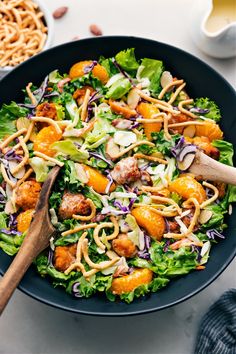 a salad with oranges, onions and dressing in a black bowl on a white table